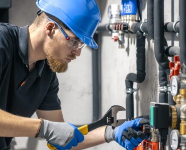 A man installs a heating system in a house and checks the pipes with a wrench. Adjusting heating valves in a residential building. A plumbing and heating technician works.