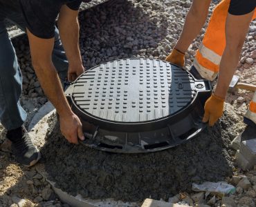 A worker installs a sewer manhole on a septic tank made of concrete rings with construction of sewerage