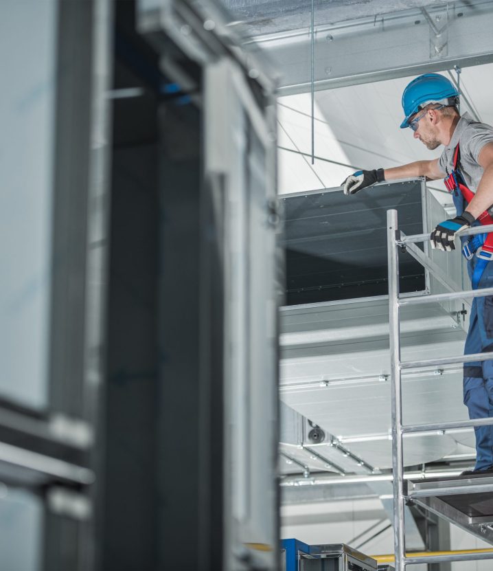 Construction Worker Checking Newly Installed Air Ventilation Shaft On Ceiling Of Large Commercial Building.