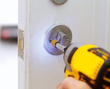 Closeup of a professional locksmith installing a new lock on a house exterior door with the inside internal parts of the lock