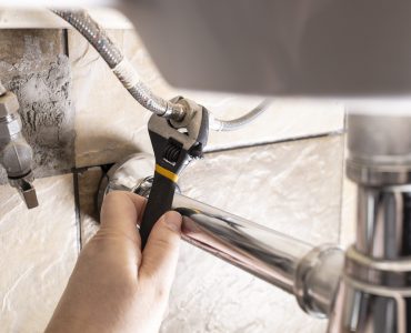 plumber hand fixes flexible hoses under sink by adjustable wrench closeup at home