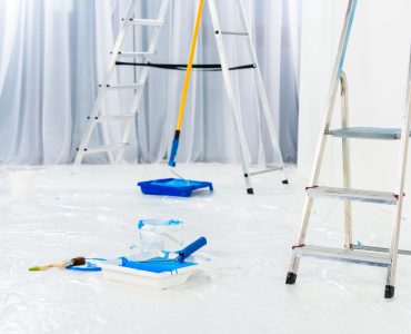 ladders and paint roller brushes in blue paint in room