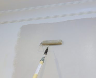 Renovation of interior, male hand painting wall with paint roller painting apartment, renovating with color paint