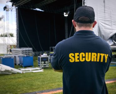 Rear View Of Security Team At Outdoor Stage For Music Festival Or Concert