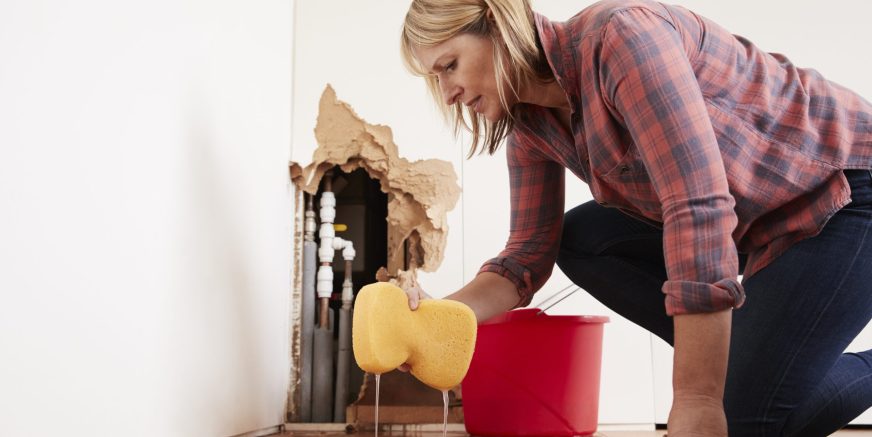Worried woman mopping up water from a burst pipe with sponge